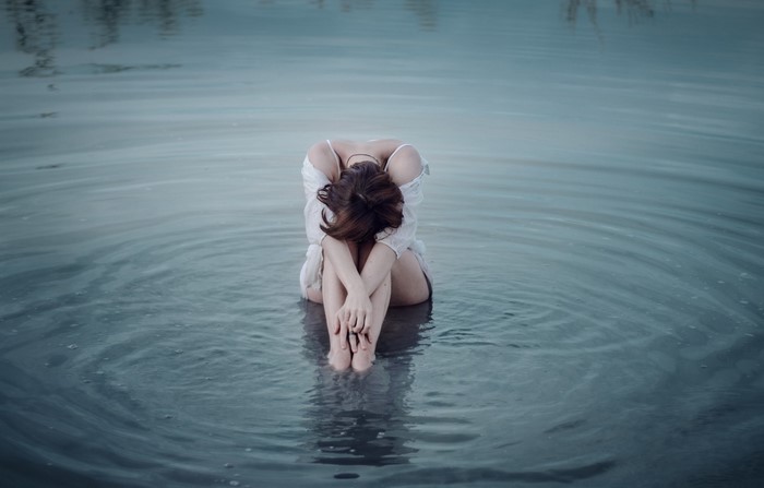 Woman sitting in water with head down