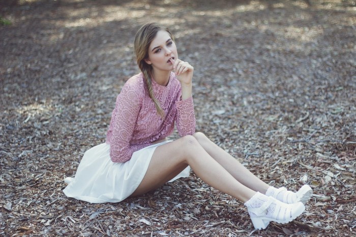 Woman in pink lace top and white skirt sitting on ground