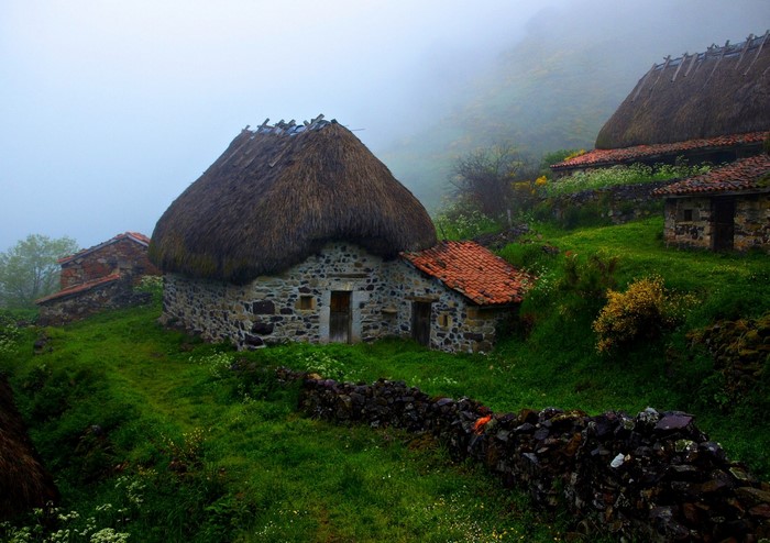 Stone houses with thatched roofs in a misty rural landscape