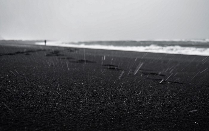 Person walking on a black sand beach in the rain