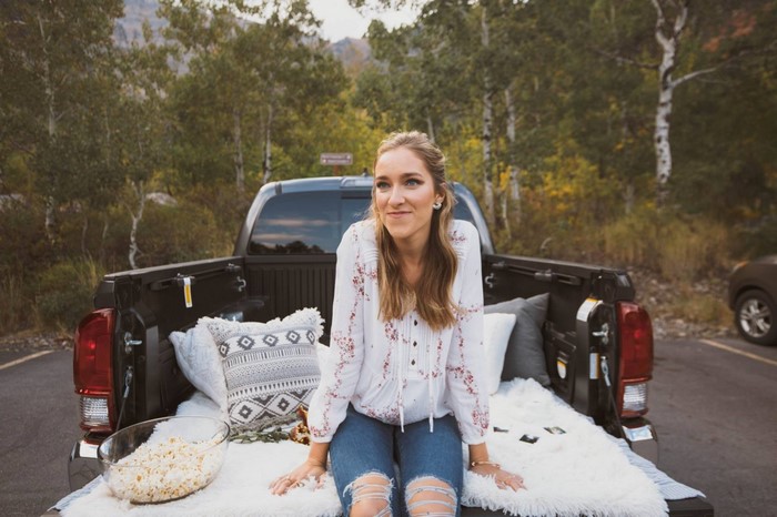 Woman sitting in the back of a truck with pillows and popcorn