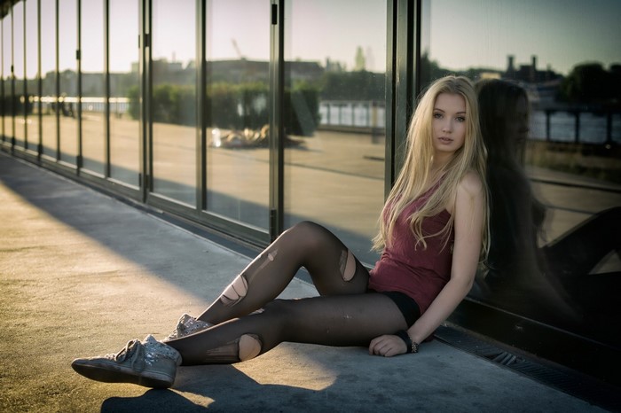 Woman in ripped tights sitting by glass building