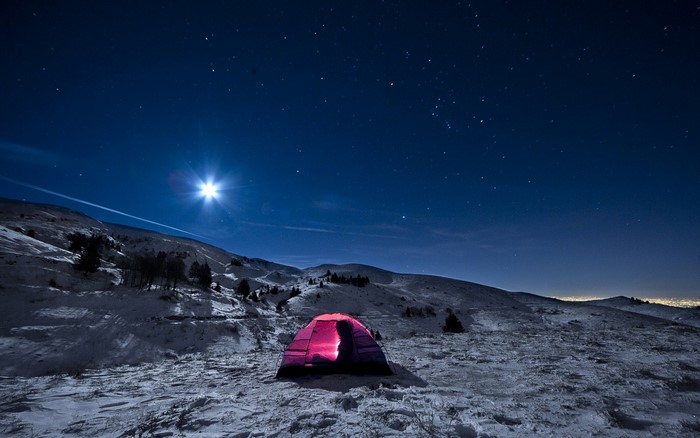 Tent under starry night sky in snowy mountains