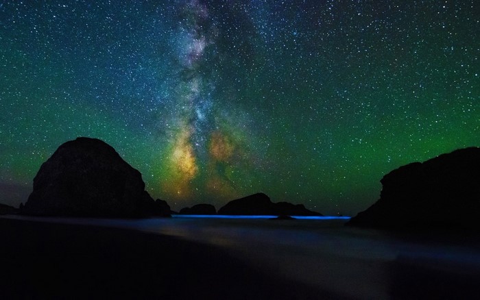 Milky Way over rocky coast with bioluminescent waves
