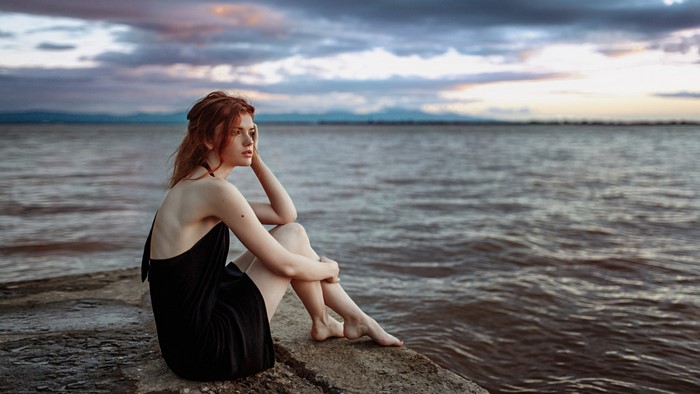 Woman with red hair sitting by the sea at sunset