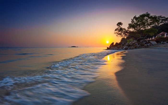 Sunset over a tropical beach with waves and rocks