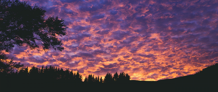 Dramatic sunset clouds over silhouetted trees and hills