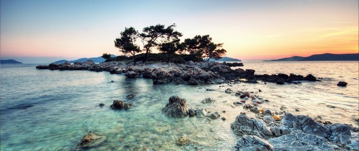 Rocky island with trees at sunset over the sea