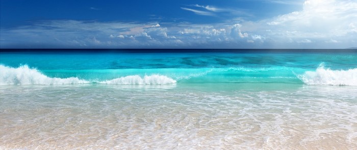 Ocean wave crashing on a sandy beach under a blue sky