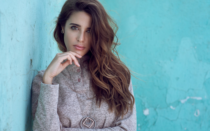 Woman with long brown hair leaning against a blue wall