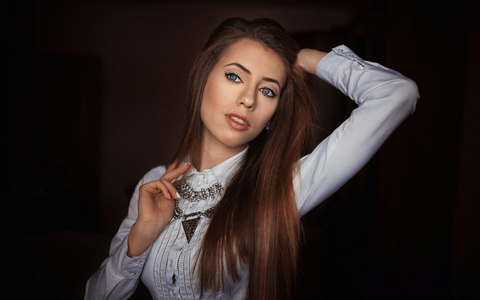 Woman with long brown hair and blue eyes wearing a white shirt and necklace