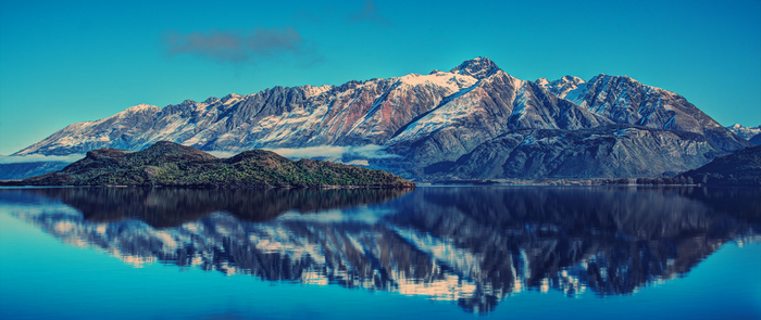 Snow-capped mountains reflected in a calm lake with an island