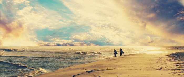 Two surfers walk along a beach at sunset