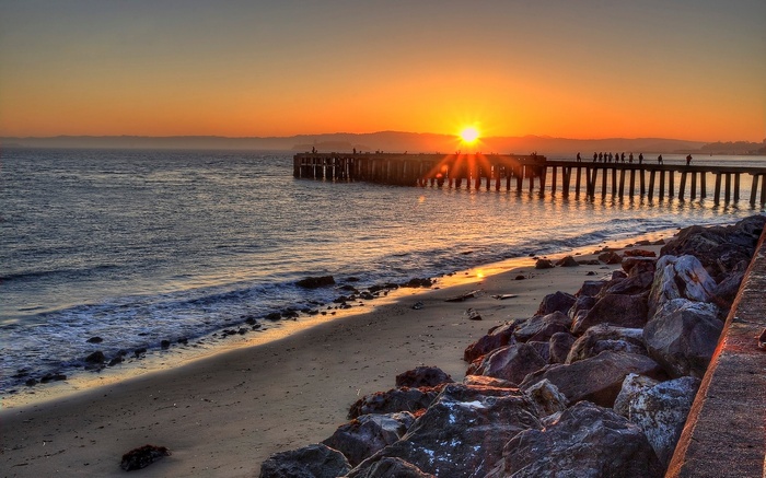 Sunset over a pier and beach with rocks