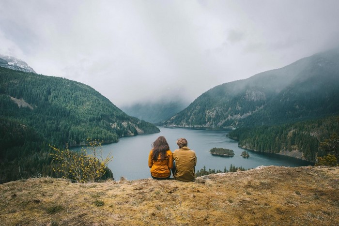 Couple sitting on a cliff overlooking a misty mountain lake