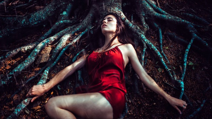 Woman in red dress lying among tree roots