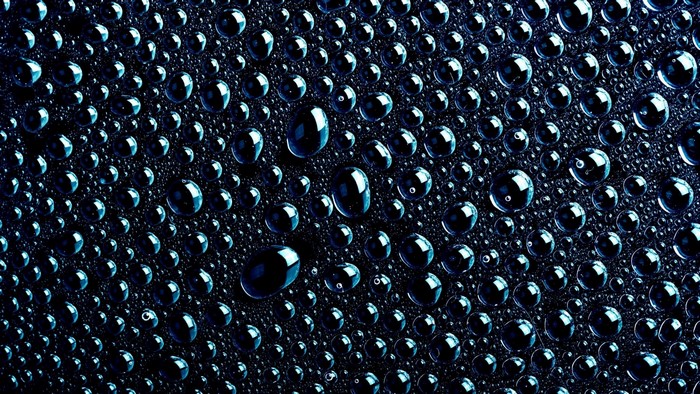 Close-up of blue water drops on a black textured surface