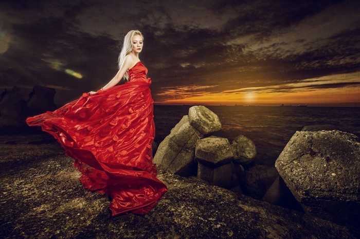 Woman in red dress on rocky shore at sunset