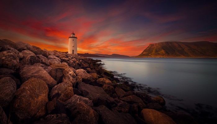 Lighthouse on rocky shore during sunset over the ocean