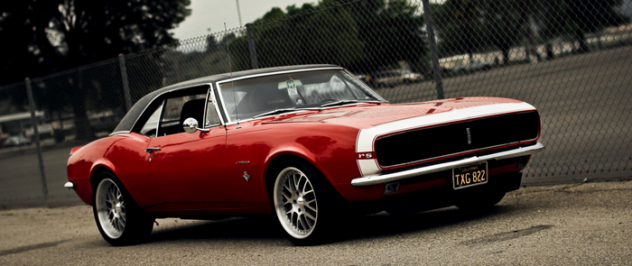 Red 1967 Chevrolet Camaro RS parked near a fence