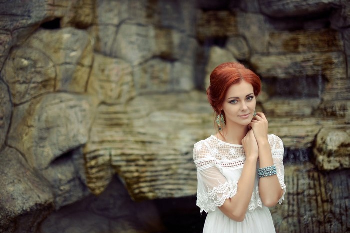Redhead woman in white dress posing in front of rock formation