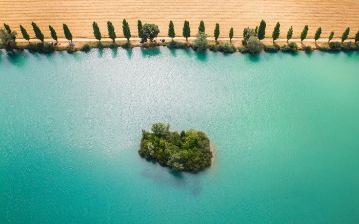 Aerial view of a small green island in a turquoise lake with a field and trees