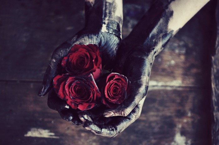Hands covered in black paint holding red roses