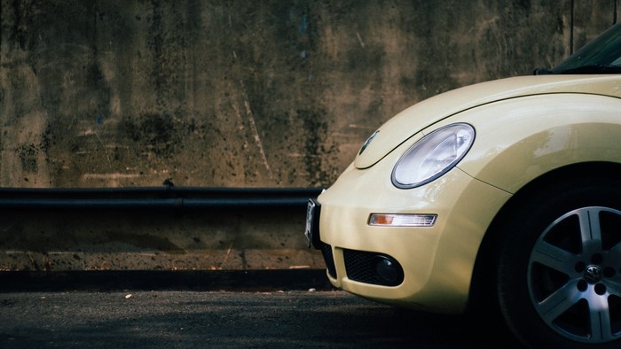 Yellow Volkswagen Beetle parked against a concrete wall