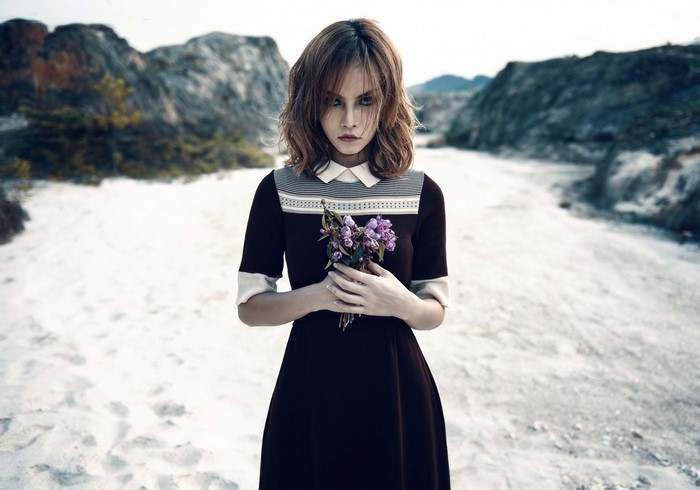 Woman in dress holding flowers in a desolate landscape