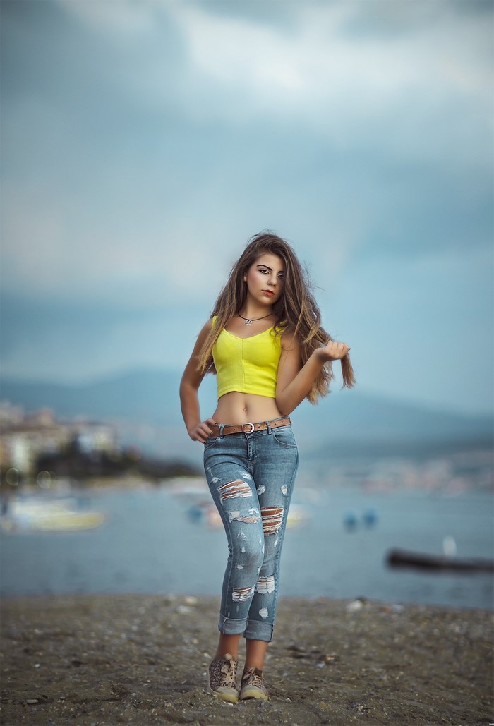 Young woman in ripped jeans and yellow crop top by the sea
