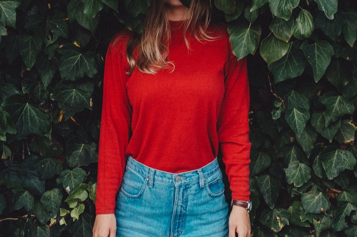 Woman in red sweater and jeans against green ivy wall