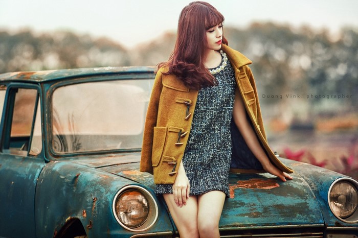 Woman in coat and dress leaning on vintage car