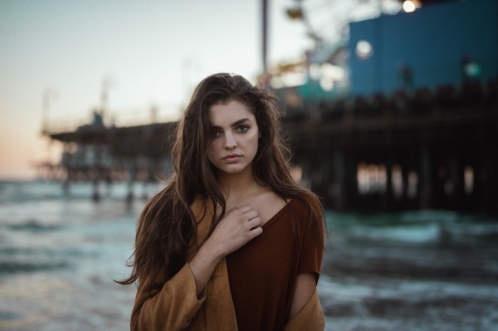 Woman with long brown hair on a beach near a pier