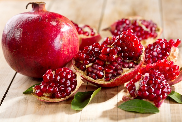 Whole and cut pomegranates on wooden surface
