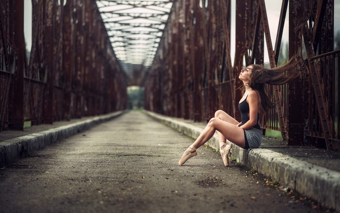 Woman in ballet slippers sitting on a rusty bridge