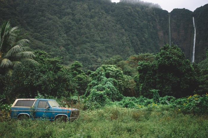 Abandoned blue car in a lush green valley with waterfalls