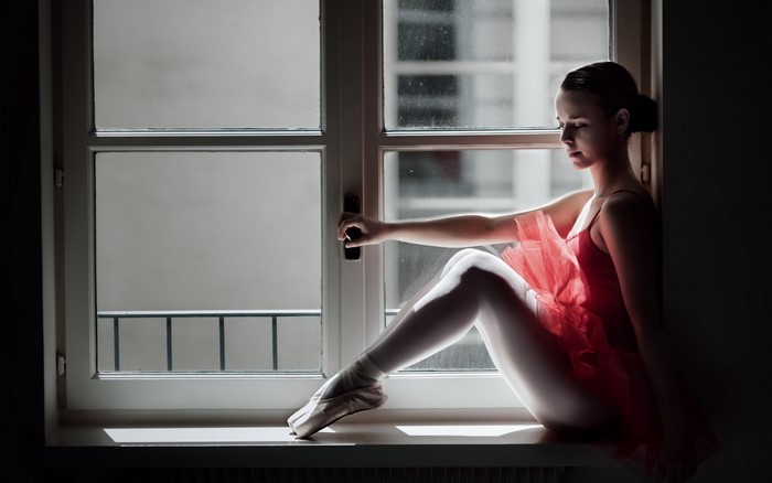 Ballerina in red dress sitting by the window
