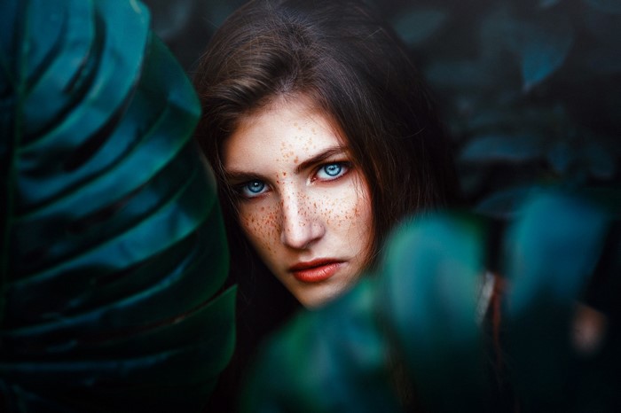 Woman with blue eyes and freckles peeking through leaves