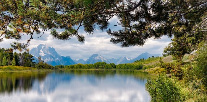 Lake reflection of mountains and trees under cloudy sky