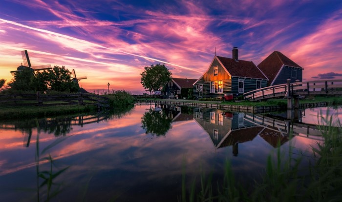 Dutch windmills and houses reflected in canal at sunset