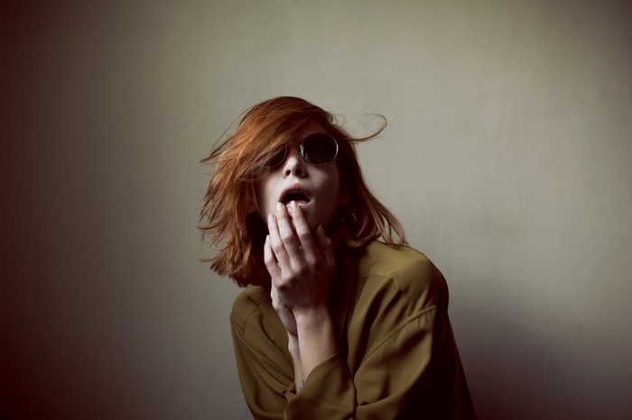 Woman with red hair wearing sunglasses and olive shirt