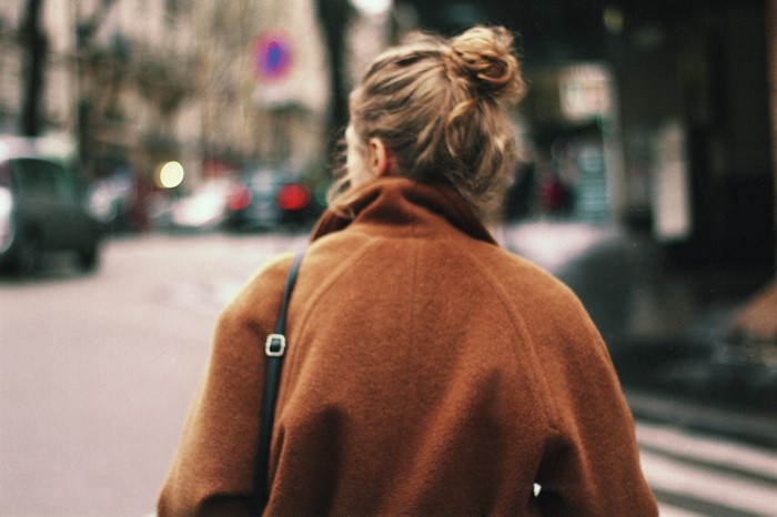 Woman with hair bun in brown coat on street