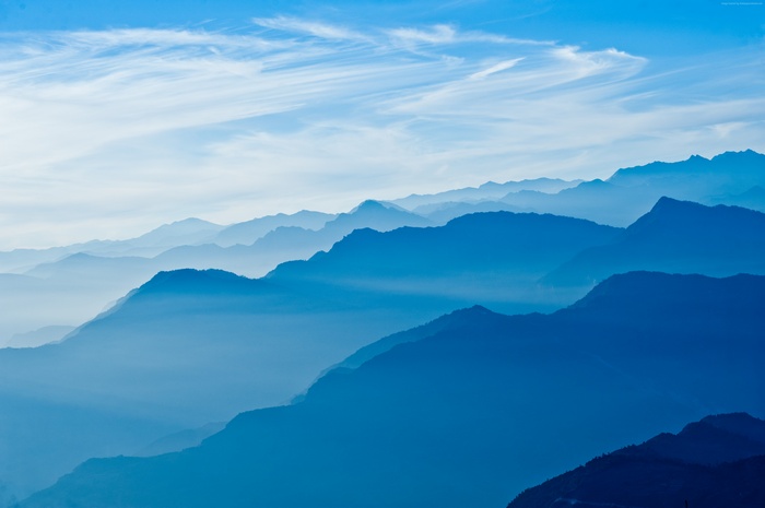 Layered blue mountains in Nepal with wispy clouds