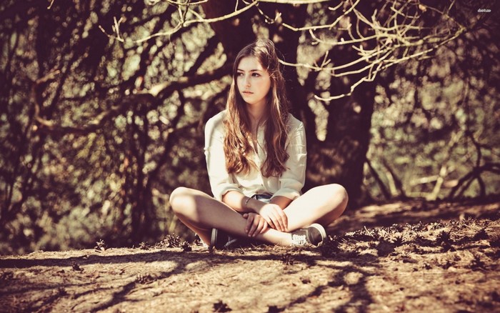 Young woman sitting cross-legged outdoors under trees