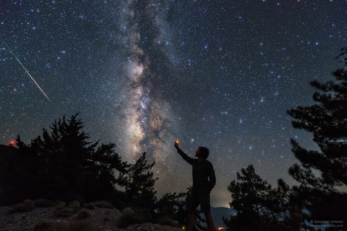 Man holding a light under the Milky Way and a meteor shower