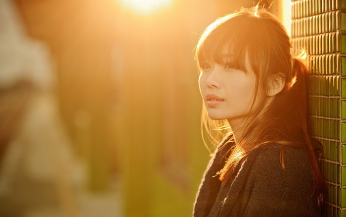 Woman with bangs in sunlight near a tiled wall