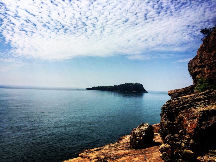 Island in the sea with rocky cliffs and clouds