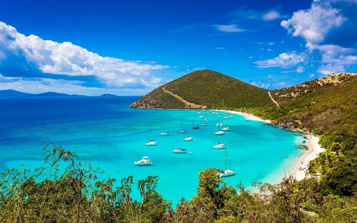 Boats anchored in a turquoise bay with a green island