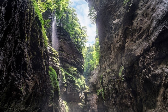 Waterfall cascading down a mossy cliff face in a deep canyon
