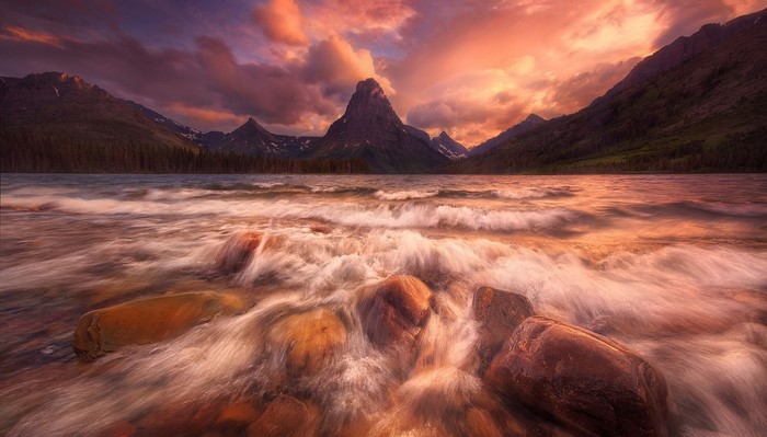 Sunset over mountains and lake with waves crashing on rocks
